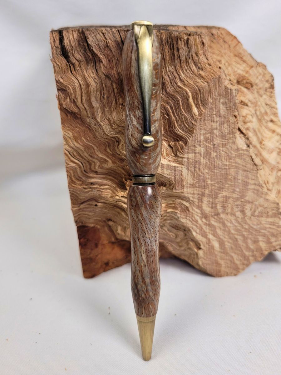 Stylo artisanal en racine de hêtre mouchetée, placage bronze, mis en valeur devant un bloc de bois naturel.