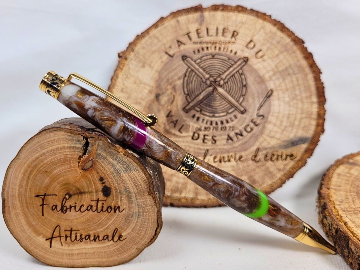 Stylo artisanal en résine époxy marbrée avec finitions dorées présenté sur rondins de bois