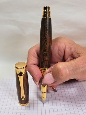 Stylo plume artisanal en hêtre teinté avec placage or et plume iridium tenu en main