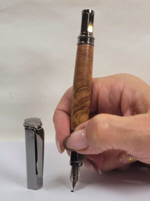Stylo plume artisanal en bois d'olivier tenu en main avec plume en iridium taille M, capuchon magnétique noir brillant retiré et détails des veinages caractéristiques de l'olivier