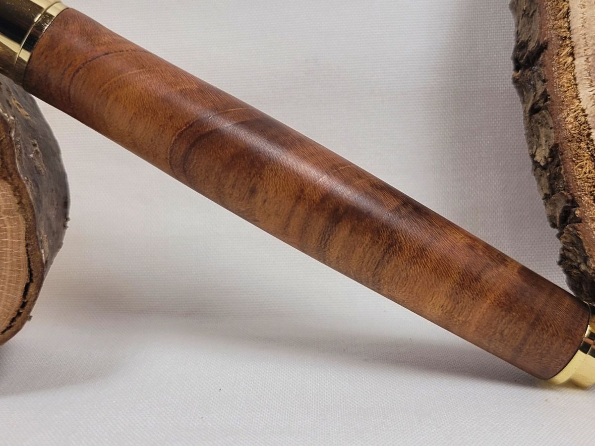 Gros plan sur le veinage naturel du bois de cerisier, révélant les fibres traversantes et les nuances chaleureuses de ce stylo roller artisanal à placage doré.