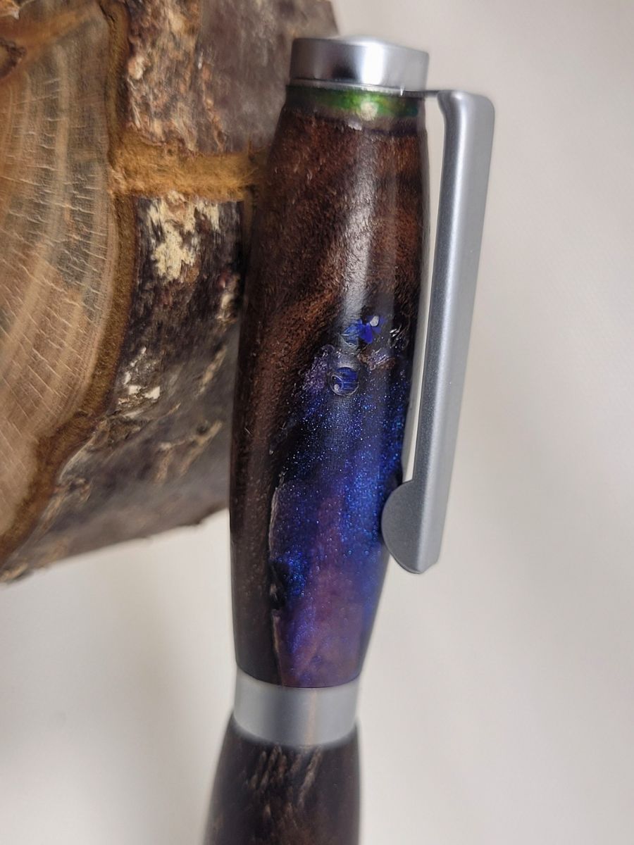 Gros plan sur un mini stylo artisanal en palissandre et résine mauve scintillante avec finition chrome mat