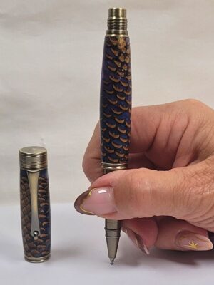 Stylo roller artisanal en résine époxy bleue et cœur de pomme de pin naturelle tenu en main, équipé d'une cartouche à bille céramique pour une écriture fine et confortable
