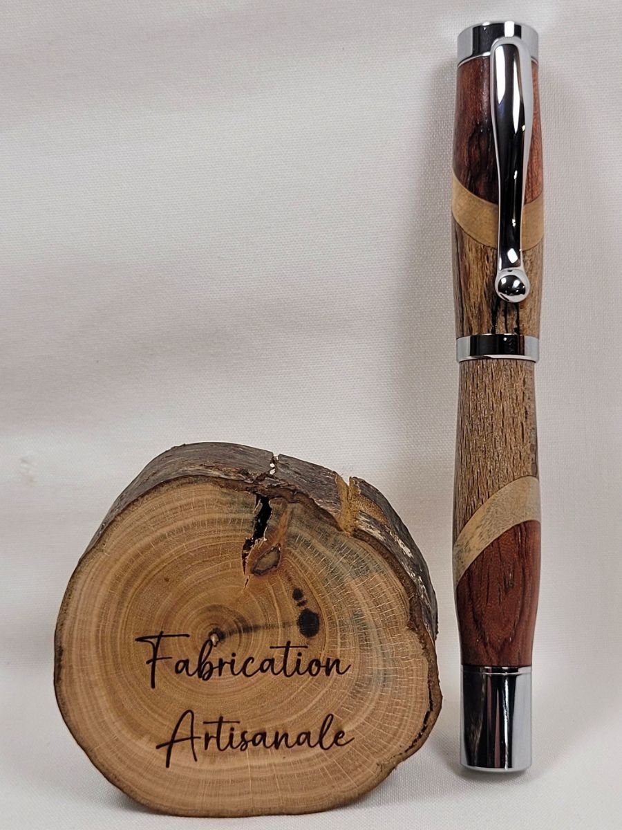 Roller artisanal en assemblage de hêtre échauffé, bouleau et padouk avec finition chromée brillante, présenté debout devant une rondelle de bois gravée fabrication artisanale, création unique réalisée à la main en Moselle.