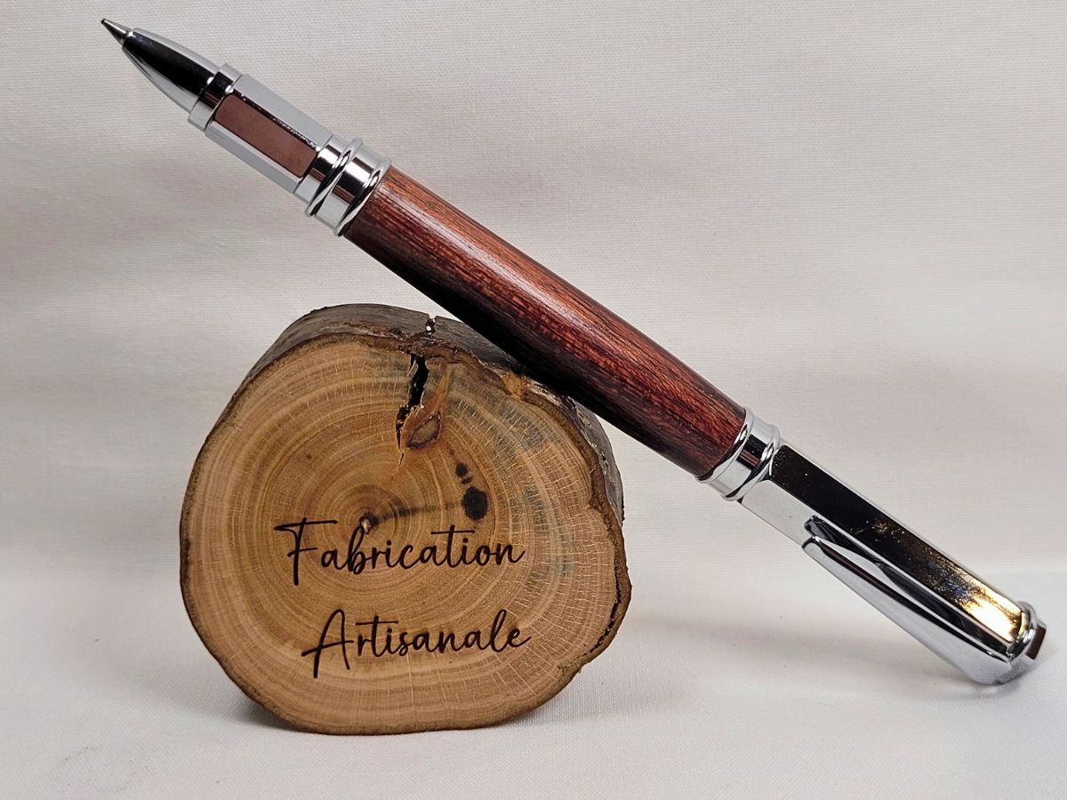 Stylo roller artisanal en bois d'amarante avec capuchon chromé, fabrication française posé sur un rondin de bois