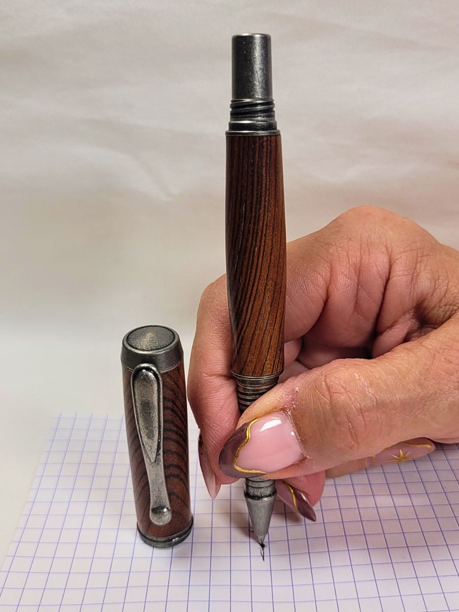 Roller artisanal en cocobolo et étain tenu en main avec écriture fine et cartouche roller céramique