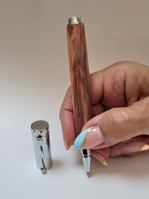 Stylo roller magnétique en hêtre échauffé stabilisé rouge avec mécanisme chromé, présenté en main pour mettre en valeur la couleur rouge du bois et la pointe roller.