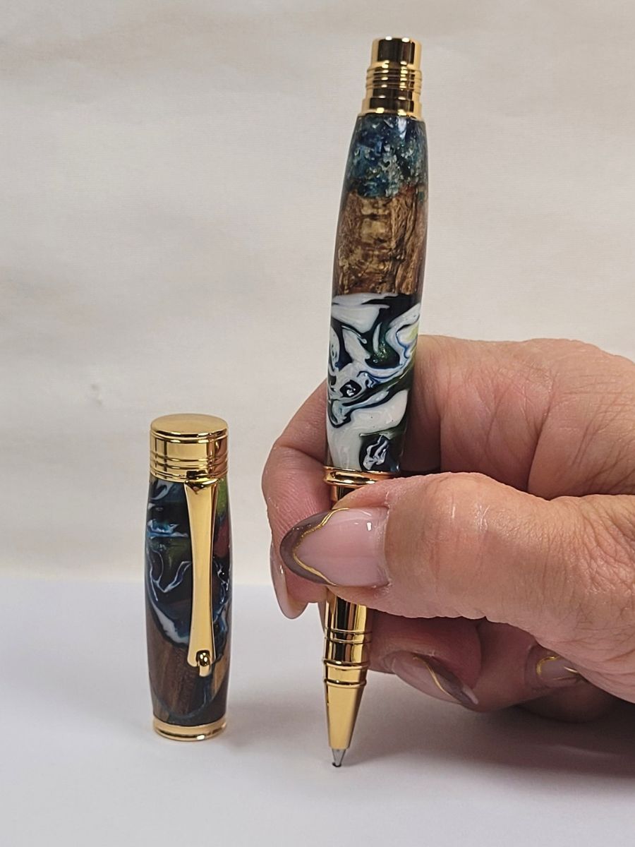 Stylo roller artisanal en bois et résine époxy tenu en main finition dorée écriture fine