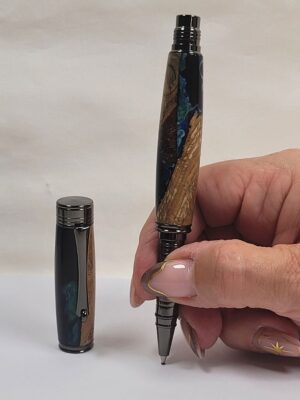 Stylo roller hybride artisanal en bois de hêtre et résine époxy bleu nuit tenu en main pour montrer ses dimensions, avec reflets bleutés et finitions plaquées noir.