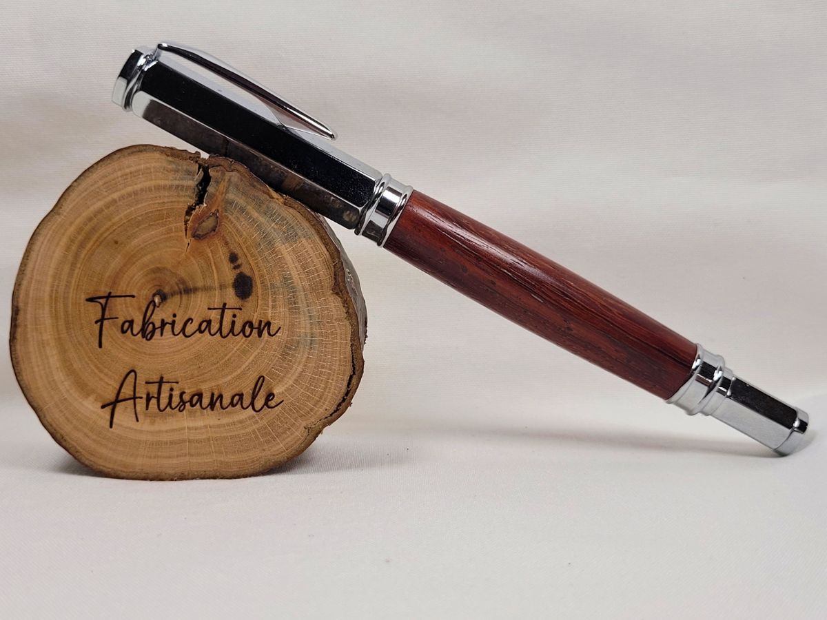 Stylo roller hexagonal magnétique en bois de padouk présenté fermé avec son capuchon chromé. Les veines naturelles du bois exotique et les reflets de la finition polie mettent en valeur cette création artisanale française réalisée à la main.