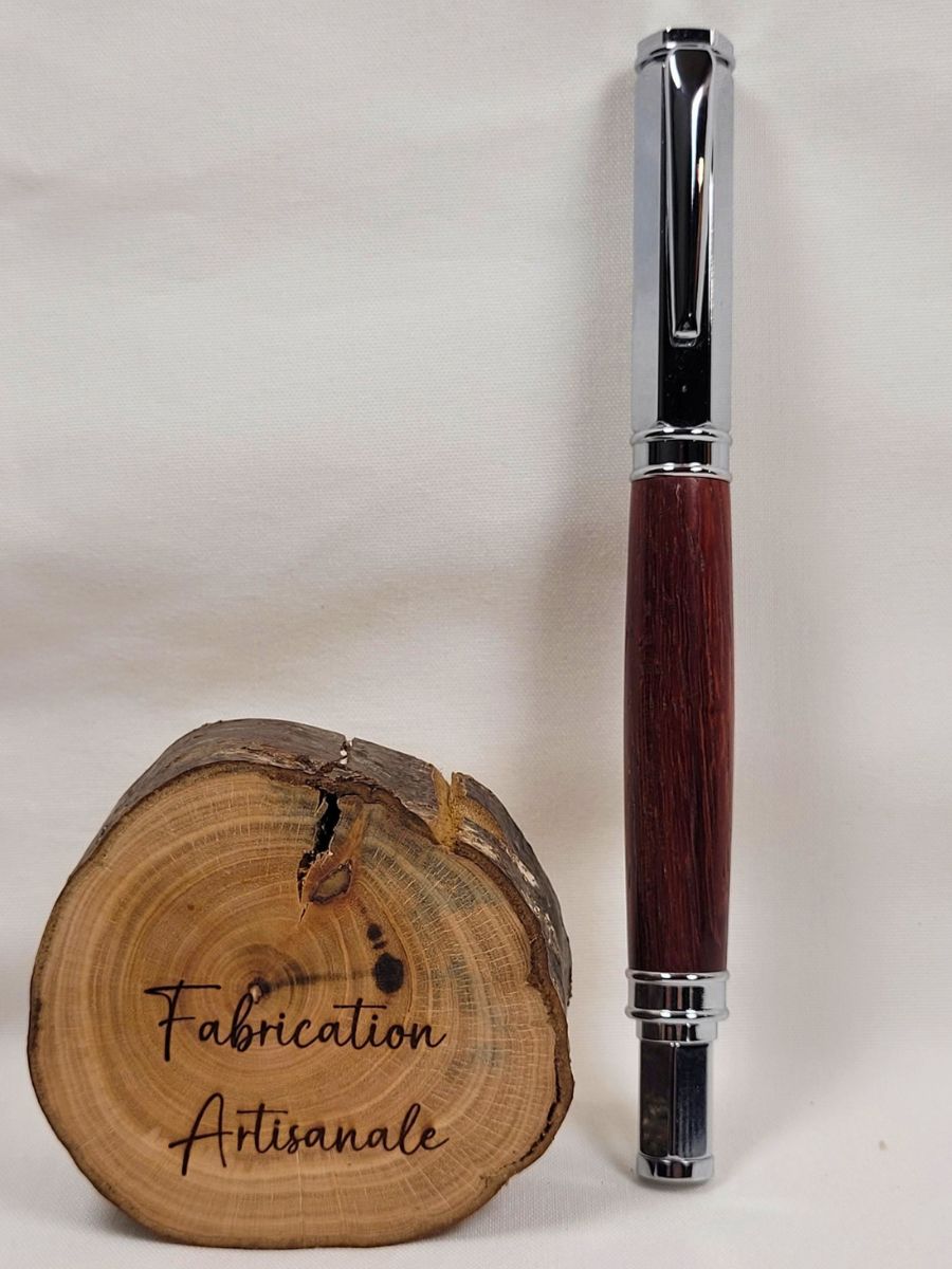 Stylo roller hexagonal magnétique en padouk avec finition chromée, présenté debout à côté d'une rondelle de bois gravée Fabrication Artisanale, création artisanale française réalisée à la main.