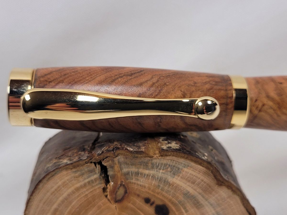 Détail du capuchon et du clip plaqués or d'un roller artisanal en bois d'olivier. La finition brillante met en valeur la richesse du veinage naturel et la qualité des finitions réalisées à la main dans un atelier français.