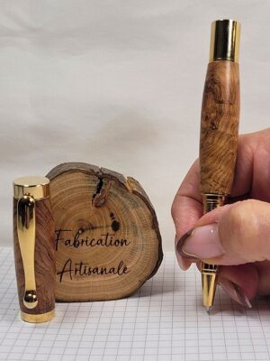 Roller artisanal en bois d'olivier tenu en main, finition plaquée or brillante, démonstration de la prise en main ergonomique et du confort d'écriture. Les dessins naturels du bois d'olivier rendent cette création artisanale française totalement unique et impossible à reproduire à l'identique.