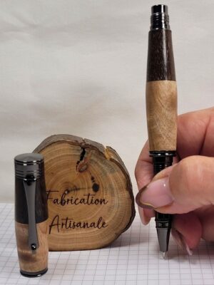 Stylo roller en bois panachés composé de bouleau ondé et de palissandre noir, présenté ouvert et tenu en main pour illustrer les dimensions réelles et le confort d'écriture. Les attributs noirs soulignent l'élégance du contraste naturel entre les deux essences.