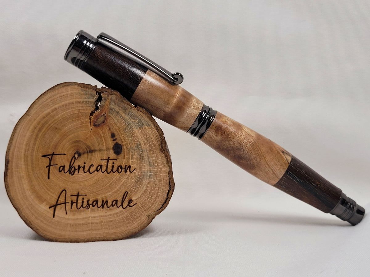 Stylo roller artisanal fermé en bois panachés assemblés, composé de bouleau ondé et de palissandre. Le montage alterné des essences crée un contraste harmonieux entre les nuances claires et foncées. Le veinage naturel du bois, la finition soignée et les éléments en placage noir confèrent à cette création un caractère authentique et raffiné. Chaque exemplaire présente des dessins de bois uniques.