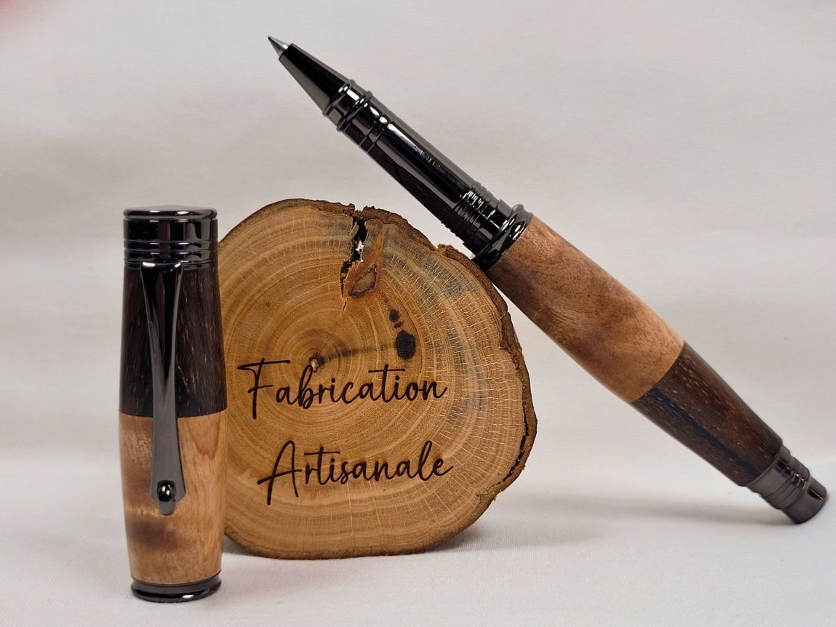 Stylo roller artisanal à capuchon vissé en bouleau ondé et palissandre noir, présenté ouvert à côté de son capuchon assorti. Les parties en bouleau ondé révèlent un veinage clair et légèrement flammé tandis que le palissandre apporte des nuances brun foncé profondes. Les attributs en placage noir brillant soulignent le contraste naturel entre les deux essences de bois. Fabrication artisanale française réalisée à la main.