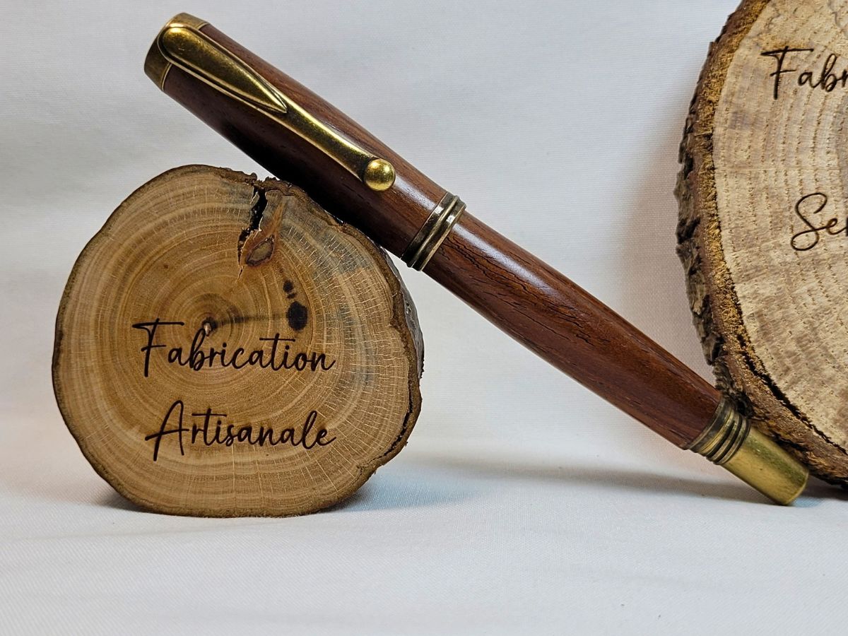 Stylo roller artisanal en padouk avec finition bronze présenté sur rondelle de bois