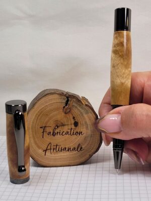 Roller artisanal en bouleau ondé tenu en main montrant la taille du stylo et la qualité des finitions noir brillant