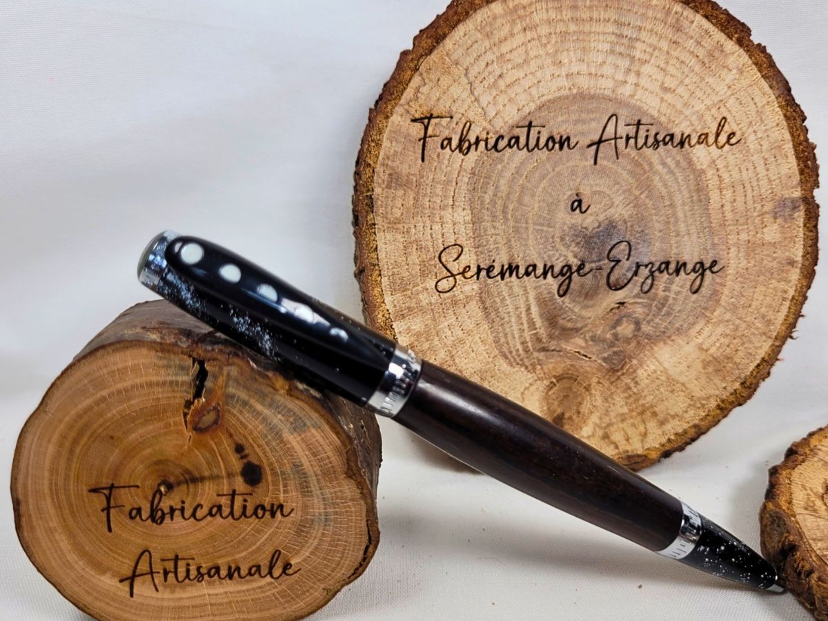 Stylo bille artisanal en ébène avec décoration galaxie chromée, phases de lune sur l'épingle, posé sur des rondelles de bois avec inscription fabrication artisanale