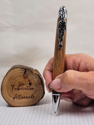 Stylo bille artisanal football en hêtre teinté tenu en main pour démonstration d'écriture, finition chrome noir et décor joueur en action