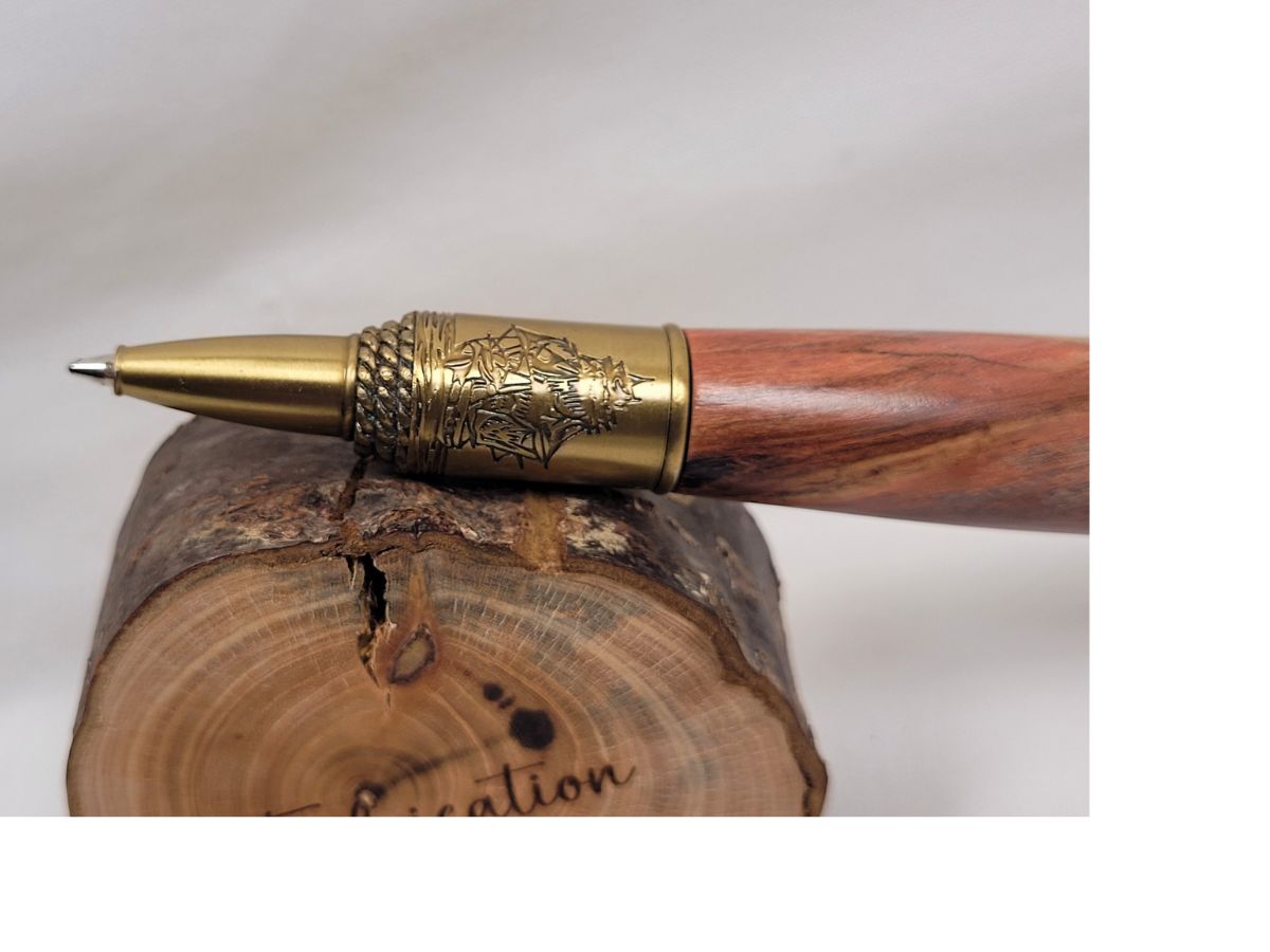 Détail de la pointe d'un stylo en bois de cerisier tourné à la main, finition laiton gravé représentant un voilier de navigation sur fond marin