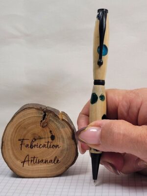 Stylo slim artisanal en bois de charme tenu en main pour montrer ses dimensions réelles, incrustations de résine multicolore réparties sur le corps du stylo, finitions noir mat, clip à épingle boule et mécanisme twist compatible recharge Cross