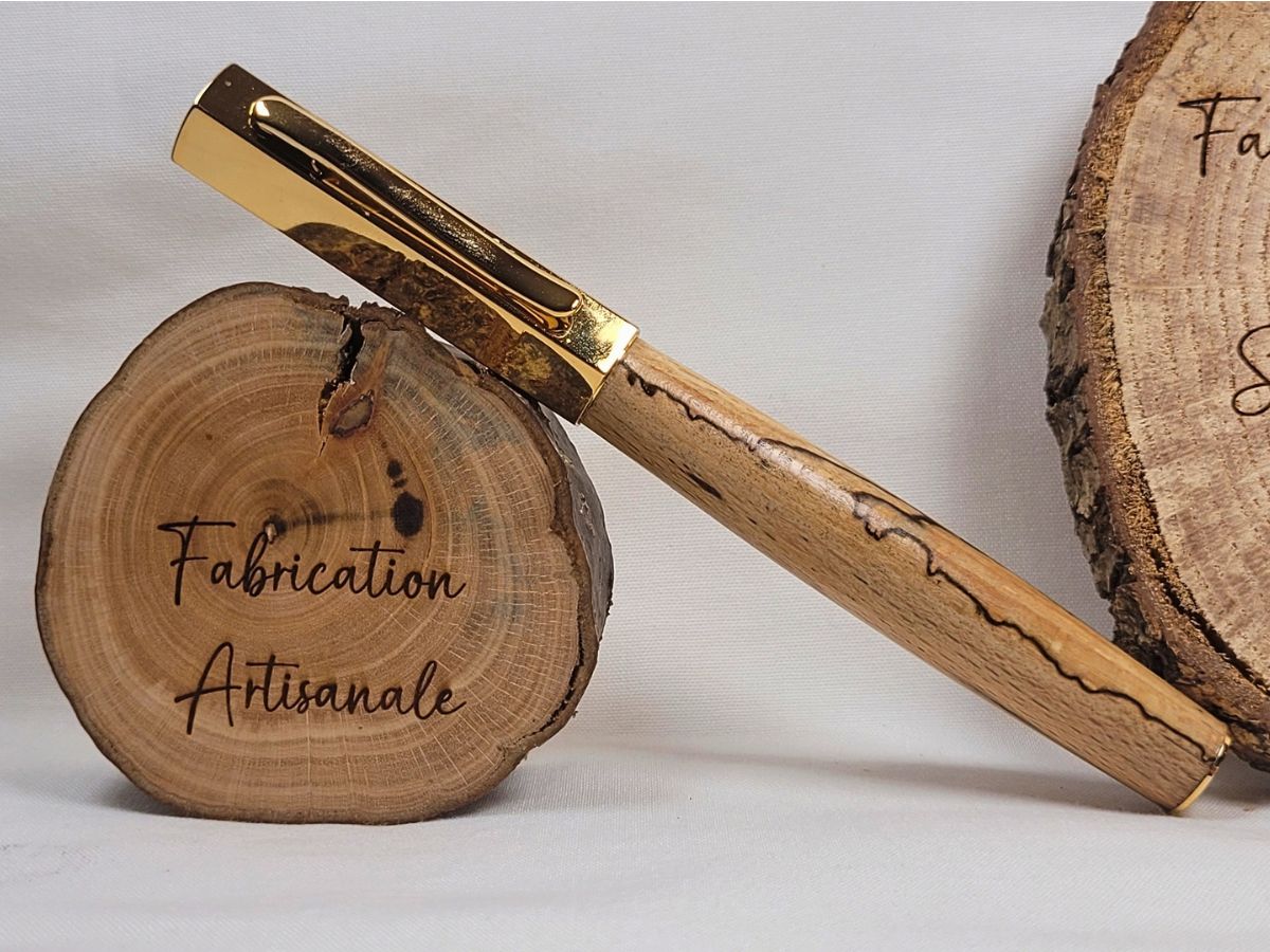 Stylo roller artisanal en hêtre échauffé avec capuchon hexagonal doré, présenté fermé pour révéler les motifs naturels du bois.