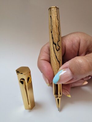 Stylo roller artisanal en hêtre échauffé avec placage doré, mettant en valeur les lignes noires naturelles du bois et le capuchon hexagonal à emboîtement.