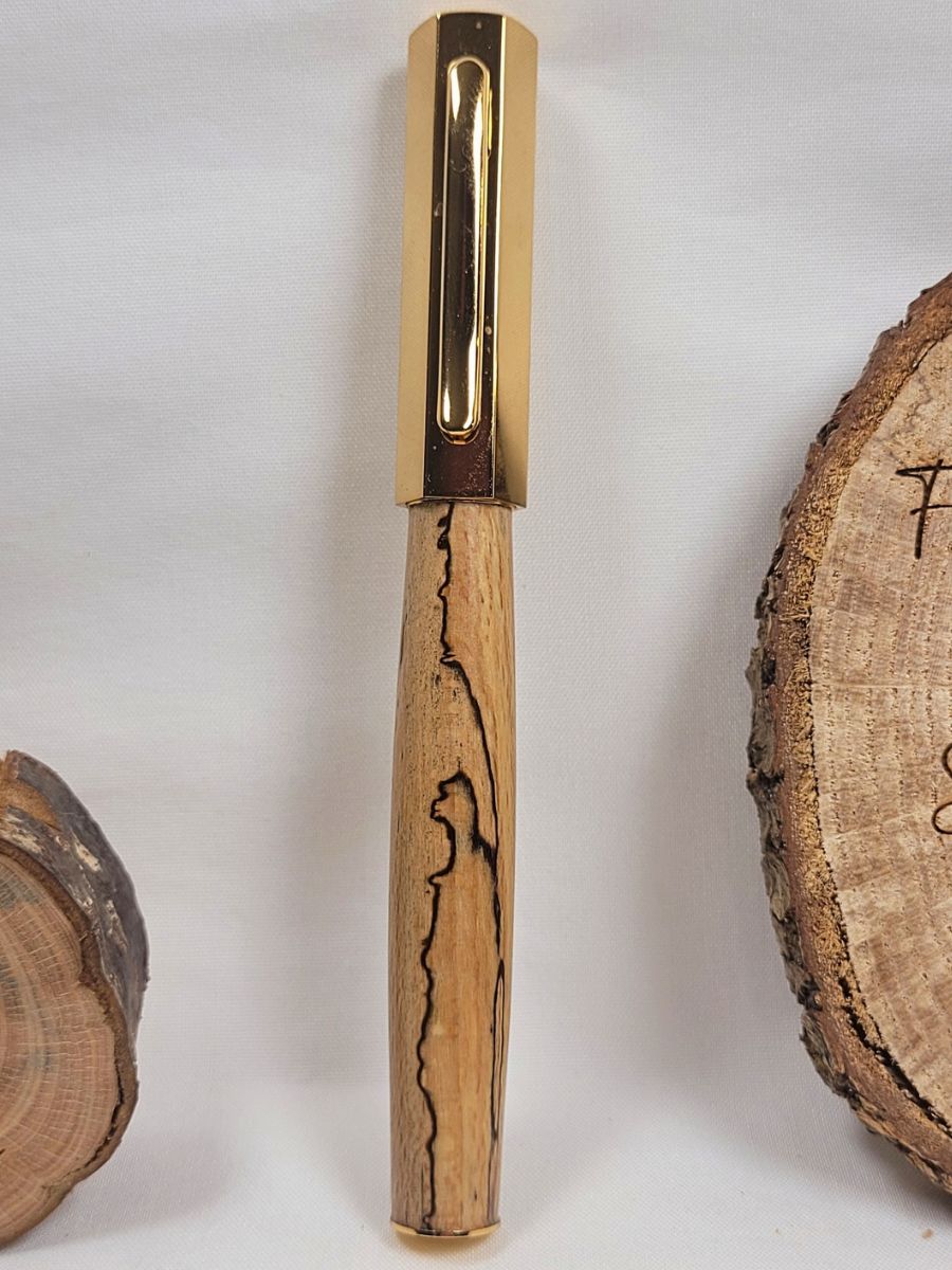 Stylo roller en hêtre échauffé et placage doré, mettant en valeur le capuchon hexagonal et les veines sombres caractéristiques du bois.