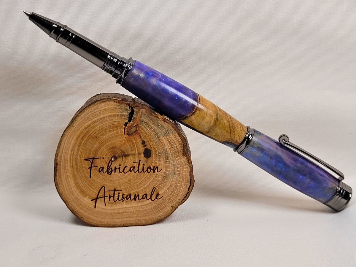 Stylo roller artisanal en hêtre et résine époxy mauve aux reflets violacés, présenté ouvert avec attributs noir brillant sur support en bois, fabrication française réalisée à la main.