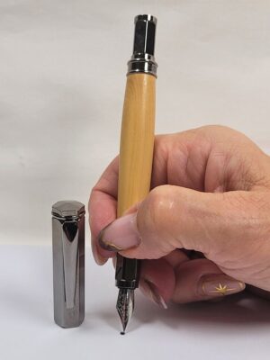 Stylo plume artisanal en bois de buis tenu en main avec plume en iridium taille M et capuchon magnétique noir brillant posé à côté